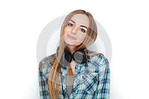 Headshot of a young adorable blonde woman in blue plaid shirt enjoying listening music to big professional dj headphones.