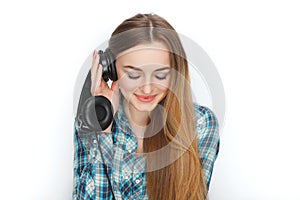 Headshot of a young adorable blonde woman in blue plaid shirt enjoying listening music to big professional dj headphones.