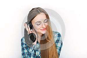 Headshot of a young adorable blonde woman in blue plaid shirt enjoying listening music to big professional dj headphones.