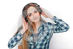 Headshot of a young adorable blonde woman in blue plaid shirt listening to big professional dj headphones.