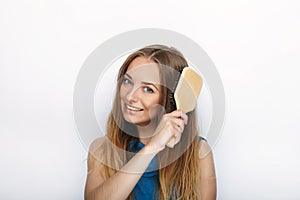 Headshot of young adorable blonde woman with cute smile with comb in hand brush her hair on white background