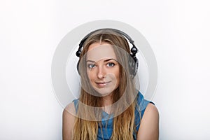 Headshot of young adorable blonde woman with cute smile wearing big black professional monitoring headphones against white studio