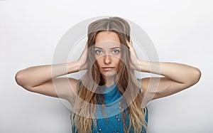 Headshot of young adorable blonde woman with cute smile on white background covers her ears with palms