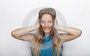 Headshot of young adorable blonde woman with cute smile on white background covers her ears with palms