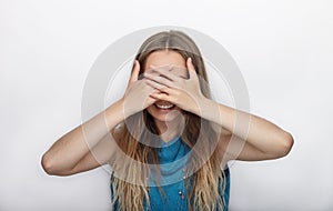 Headshot of young adorable blonde woman with cute smile on white background covers her face with palms