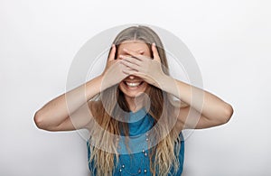 Headshot of young adorable blonde woman with cute smile on white background covers her face with palms