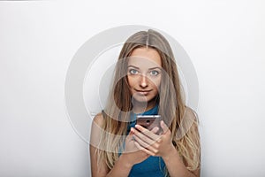 Headshot of young adorable blonde woman with cute smile on white background texting on her smartphone