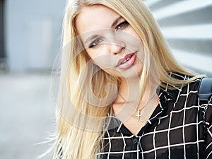 Headshot of young beautiful excited woman with gorgeous natural lips, blue and brown eyes in black blouse on urban metal strips ba