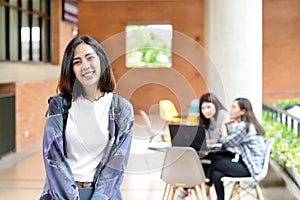 Headshot of young happy attractive asian student smiling and looking at camera with friends on outdoor university background.