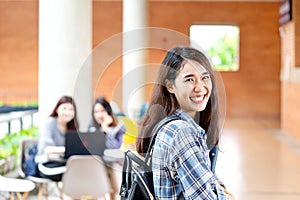 Headshot of young happy attractive asian student smiling and looking at camera with friends on outdoor university background.