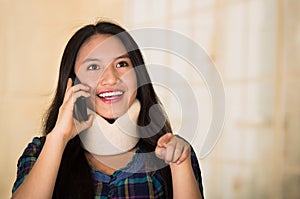 Headshot young hispanic woman posing wearing neck brace, smiling happily while talking on phone, injury concept