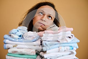 Headshot young mother holding up a stack of washed, ironed baby clothes, sighing and looking tired from household chores