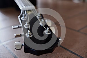 Headstock and tuners of beautiful black acoustic guitar lying on the brick floor closeup.