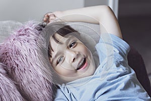 Healhty kid smiling face lying head on fulffy cushion, Happy child boy relaxing at home enjoying time on his own. Positive