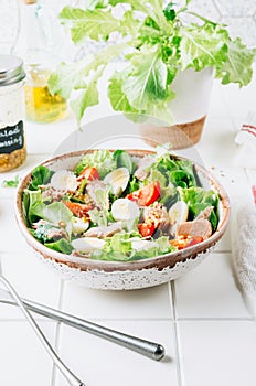 Healhty tuna salad with tomato, quail eggs, lettuce and salad dressing with olive oil, lemon juice and grain mustard.