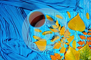 Healing cup of tea in a scarf on blue wooden background wiyh autumn leaf