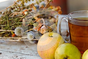 healing herbs bouquet, cup of herbal tea and some fresh fruits, apples and pears on rustic background