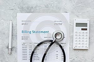 Health care billing statement with doctor`s stethoscope and pen on stone background top view