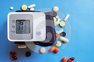 Health care. Closeup of wrist blood pressure monitor with colorful pills on blue background for medical design