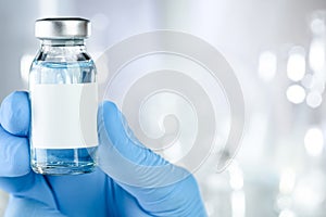 Health care concept with a hand in blue medical gloves holding a vaccine vial with blue liquid and black white label