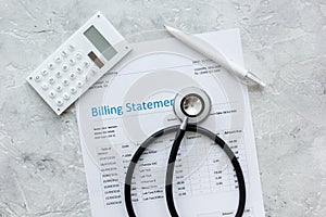 health care costs with billing statement, stethoscope and calculator on stone table top view