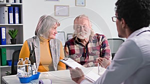 health care, elderly couple at reception of a black male doctor in a medical office