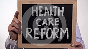 Health care reform text on blackboard in doctor hands, state government policy