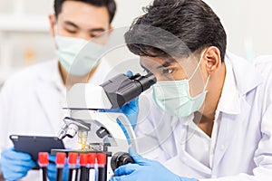 Health care researchers working in biological science laboratories, a researcher uses a microscopic and his assistant using a