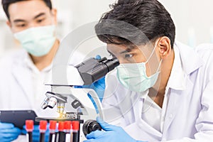 Health care researchers working in biological science laboratories, a researcher uses a microscopic and his assistant using a