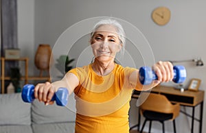 Health care, sport and active lifestyle. Happy senior woman doing exercises with dumbbells in living room interior