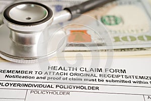 Health claim form with stethoscope and US dollar banknotes, insurance accident medical concept