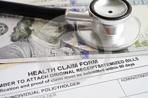 Health claim form with stethoscope and US dollar banknotes, insurance accident medical concept