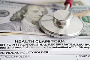 Health claim form with stethoscope and US dollar banknotes, insurance accident medical concept