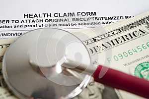 Health claim form with stethoscope and US dollar banknotes, insurance accident medical concept