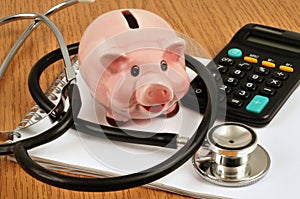 Health cost concept with piggy bank, stethoscope and calculator lying on spiral notebook