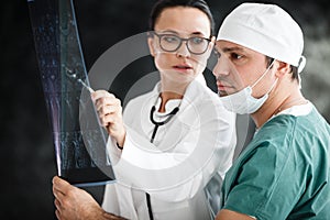 Health diagnostic in hospital. male surgeon in mask and female doctor or nurse with stethoscope reviewing x-ray scan