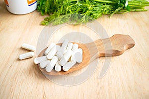 Health effects of coagulations vitamin. White capsules of vitamin K (phylloquinone) in wooden spoon on a background of a bottle o