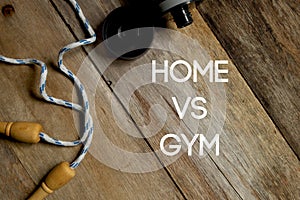 Health and fitness concept. Top view of skipping rope and water bottle on wooden background written with Home Vs Gym.