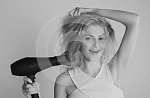 Health hair and beauty concept. Girl with blonde hair using hairdryer. Young attractive happy laughing blonde woman with