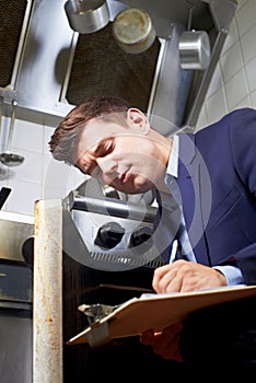 Health Inspector Looking At Oven In Commercial Kitchen