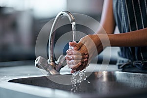 The health inspector would be very proud. a woman washing her hands in the sink of a commercial kitchen.