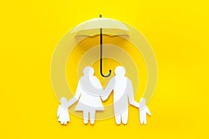 Health insurance concept. Family cutout under umbrella on yellow background top-down copy space