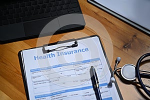 Health insurance form and stethoscope on wooden table.