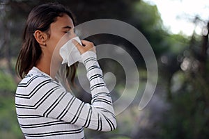 Health and medicine concept - Young woman blowing nose into tissue on the forest
