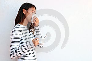 Health and medicine concept - Young woman blowing nose into tissue on white background