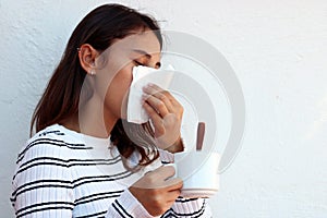 Health and medicine concept - Young woman blowing nose into tissue on white background