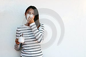 Health and medicine concept - Young woman blowing nose into tissue on white background