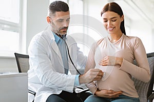 Health of the pregnant woman and baby. Male doctor listening to baby heart during young lady appointment in hospital