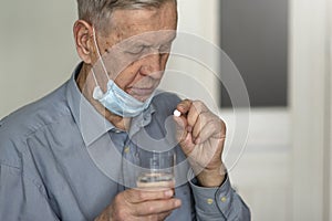 An elderly man in a medical mask takes a pill.