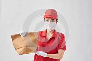 Health protection, safety and pandemic concept - delivery woman in protective face mask with food in paper bag over pink